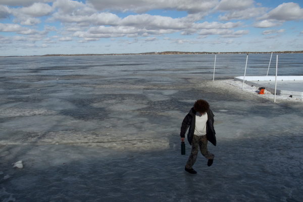 Person standing on frozen lake, glancing down at the ice.